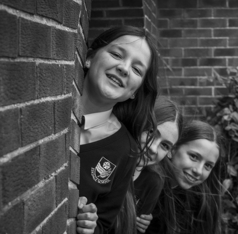 three students peering behind a wall smiling