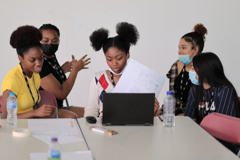 Group of students working around a laptop looking focused while mentoring takes place